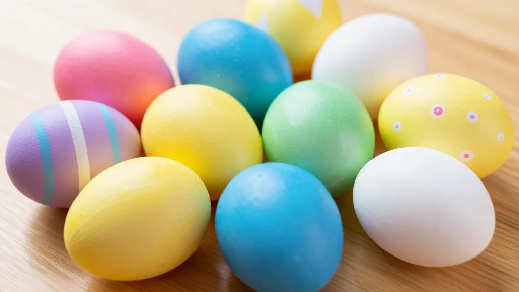 A bright, close-up photo of a collection of Easter eggs on a wooden table, featuring solid glossy colors on some eggs, clean geometric patterns with crisp tape-edged triangles and diamonds on others, and a few eggs with evenly spaced small dot patterns using a cotton swab; soft natural lighting, slight shallow depth of field to emphasize the texture of the painted shells and the smooth shine of the finishes, no text or logos.